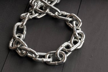 Karanlık bir zemin üzerinde parlak çelik bir zincir bir döngü şeklinde uzanır. çelik tasma