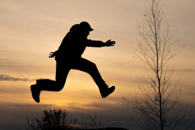 Uçan bir adamın silueti ve yaprakları olmayan bir ağacın silueti, sonbahar kaçakları