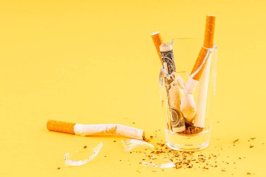 Sarı bir arka planda, içinde sigara olan bir camda. Sigara içerken sağlık sorunları