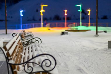 Bir kış parkındaki karla kaplı banklar, LED lambaların çok renkli ışıklarıyla aydınlatılıyor.