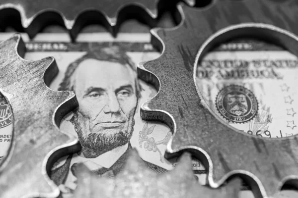 a portrait of Lincoln on a five-dollar bill, pinned on both sides by gears. dollar in trouble