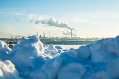 Zararlı bir üretimin kar yığınının arkasından sigara içilen bir bitki görüntüsü. Çevreye bir sürü emisyon