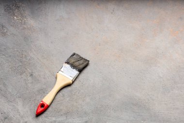 Gri tuval üzerinde eski boya fırçası. Eşit olmayan boyalarla kaplı. Gri arka planda ahşap saplı boya fırçası