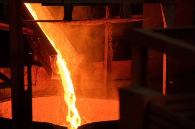 Fırından çıkan erimiş metaller kanaldan fıçıya dökülüyor. Üretim için sıcak metal püskürtülüyor.