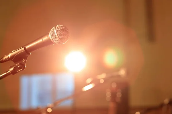 Konser ışıkları ve mikrofonun arkasında turuncu ışıklar olan parlak bir sahneye odaklanmış bir mikrofon.