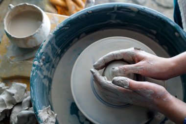 Çömlekçinin ellerinin üst görüntüsü. Bir kil ustası çömlekçi çarkında bir ürün yaratır. gri kil