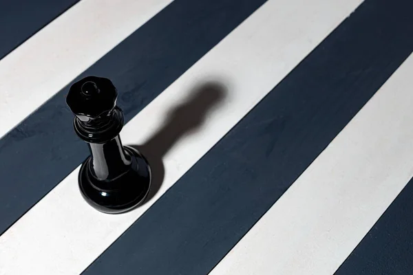 black chess piece queen casts a shadow diagonally. stripes are black and white. a different game. not like everyone else