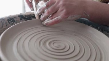 Çömlekçinin çarkındaki gelecekteki tabağın yakın çekim rotasyonu. Bir levhanın yüzeyinde güzel bir şekil yaratma süreci. Bir çömlekçinin büyüleyici çalışması