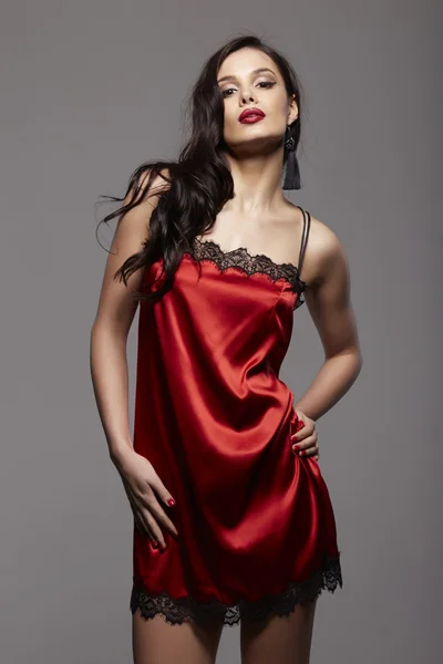 Uzun siyah saçlı ve dantel ve siyah küpe ile kırmızı gece elbiseli kırmızı dudaklar esmer kadın seksi moda — Stok fotoğraf