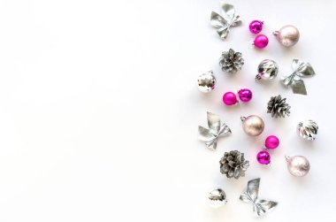 Gümüş ve pembe süslemelerden oluşan bir Noel evi. Beyaz arkaplanda toplar, koniler ve yaylar, metin için boşluk