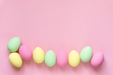 Paskalya düzlüğü. Pembe arkaplanda pastel renklerle boyanmış yumurtalar, metin için boşluk