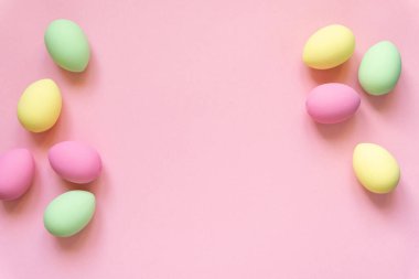 Paskalya düzlüğü. Pembe arkaplanda pastel renklerle boyanmış yumurtalar, metin için boşluk
