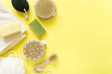 Banyo için ürünler ve eşyalar. Masaj fırçaları, sabun, sünger taşı ve sarı arka planda havlu, kopyalanma alanı
