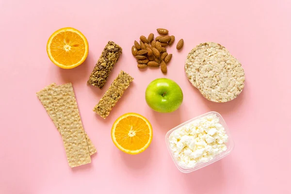 Flach lagen gesunde Snacks. Obst, Müsliriegel, Knäckebrot, Quark und Nüsse auf rosa Hintergrund, Ansicht von oben Stockfoto