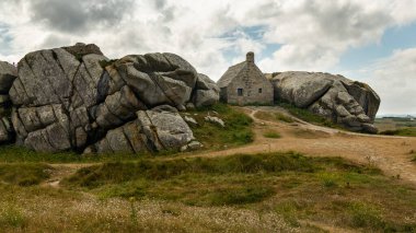 Kuzey Brittany 'deki Atlantik kıyısındaki Meneham' da kayaların arasındaki ev, yazın bulutlu bir gün.