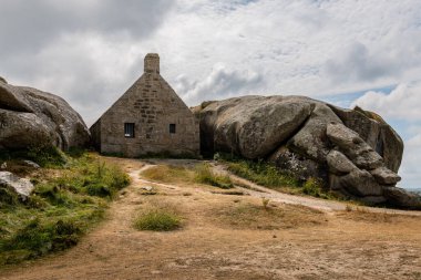Kuzey Brittany 'deki Atlantik kıyısındaki Meneham' da kayaların arasındaki ev, yazın bulutlu bir gün.
