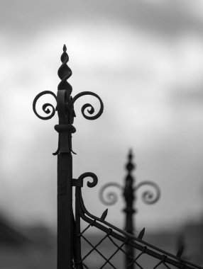 Demir çitin tepesindeki siluet, bulutlu gökyüzü.