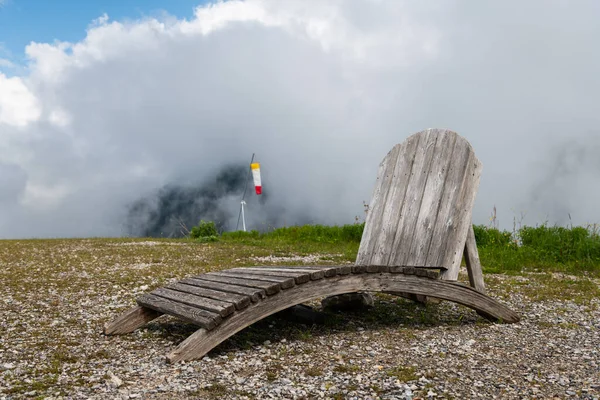 A rustic lounge chair made of wood on the top of a hill, cloudy day in spring in the Austrian Alps