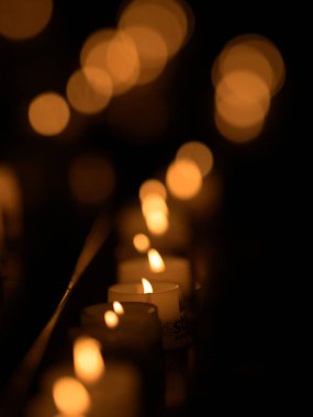 Koyu arkaplan ve diğer alevlere karşı odak noktasında yanan adak mumları.