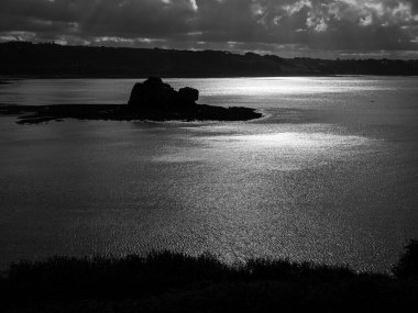 Trebeurden Fransa 'nın siyah ve beyaz kayalık kıyıları. Denize yansıyan güneş ışığı dramatik atmosferi gösteriyor.