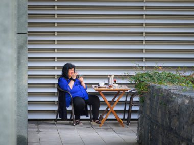 Viyana, Avusturya - 8 Eylül 2022: Mavi bluzlu bir kadın güneşli bir sonbahar gününün erken saatlerinde masada oturup akıllı telefonuna bakar