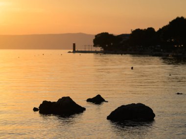 Hırvatistan 'ın Cres kentinde, deniz üzerinde canlı bir günbatımı, kırmızı deniz feneri ve kayalar, bahar mevsiminde dramatik renkler gösteriyor..
