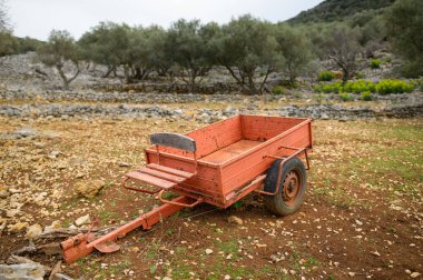 Hırvatistan 'ın Cres kentinde ilkbaharda kırsal atmosferde yakalanan taş duvarlarla çevrili küçük bir tarlada turuncu bir römork duruyor..