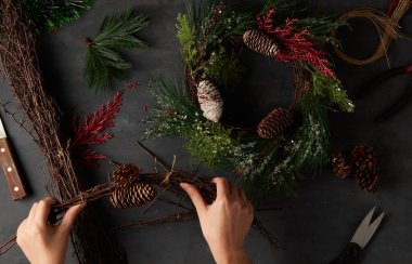 Karanlık bir arka planda Noel tacı hazırlayan kadının elleri, DIY