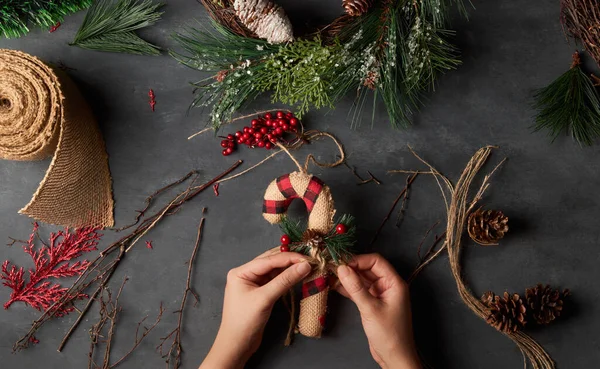 Karanlık bir arka planda Noel bastonu yapan bir kadının elleri, DIY
