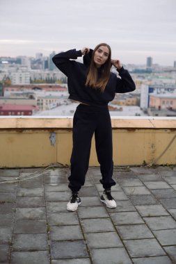 Geniş şehirde yüksek bir binanın çatısında duran genç bir kadının tam boy fotoğrafı..