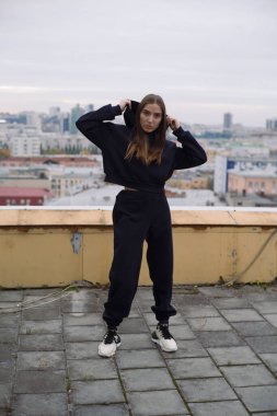 Geniş şehirde yüksek bir binanın çatısında duran genç bir kadının tam boy fotoğrafı..
