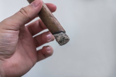 Bir adamın eli hafif bir arka planda yanan bir puro tutar.