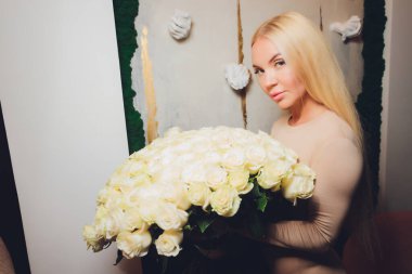 Güzel bir kadın doğum günü partisi için bir hediye ve güzel bir fotoğraf çekmek için çiçekler aldı. Şık bir beyaz ceket ve aksesuar giyiyor. Büyük dudaklar, beyaz dişler, çıplak makyaj..