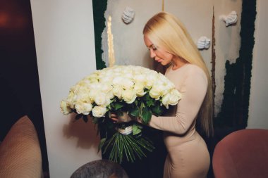 Güzel bir kadın doğum günü partisi için bir hediye ve güzel bir fotoğraf çekmek için çiçekler aldı. Şık bir beyaz ceket ve aksesuar giyiyor. Büyük dudaklar, beyaz dişler, çıplak makyaj..