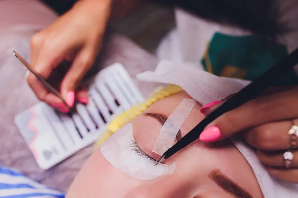 Bunch of artificial eyelashes in tweezers. Extensions of artificial eyelash, process close up. Woman in a beauty salon. Beauty and self-care.