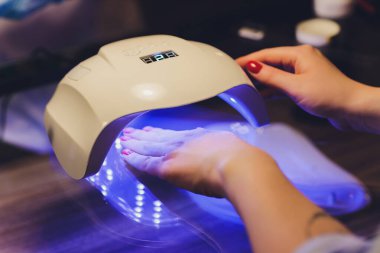 Renkli cila uygulayan güzellik uzmanının yakın çekimi. Tırnaklarına oje sürüyorum. Tırnaklarına oje sürmek için fırça sürüyorum. Güzellik salonunda manikür manikür uygulayıcısı. Güzellik salonunda vernikte.