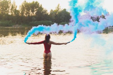 Nehir kenarında poz veren kırmızı mayolu güzel bir genç kadın. Yaz yaşam tarzı. duman bombası