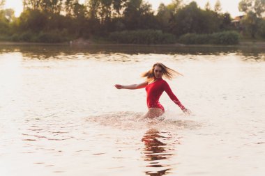 Nehir kenarında poz veren kırmızı mayolu güzel bir genç kadın. Yaz yaşam tarzı.