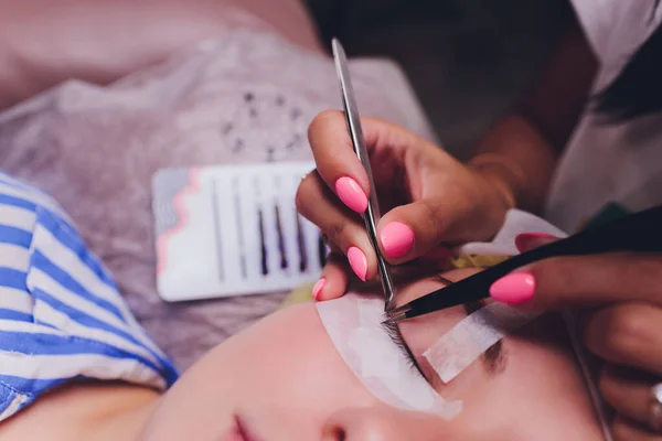 Bunch of artificial eyelashes in tweezers. Extensions of artificial eyelash, process close up. Woman in a beauty salon. Beauty and self-care.