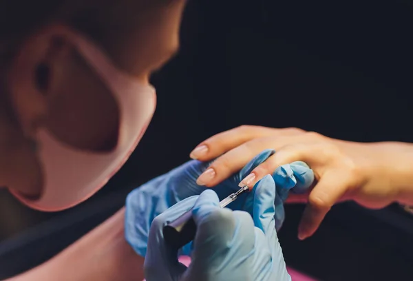 Nahaufnahme einer Kosmetikerin, die bunten Lack aufträgt. Das Auftragen von Nagellack auf die Nägel mit einem Pinsel zum Auftragen von Nagellack auf die Finger. Maniküre Nagelapplikator in einem Schönheitssalon. In einem Schönheitssalon Lack. — Stockfoto