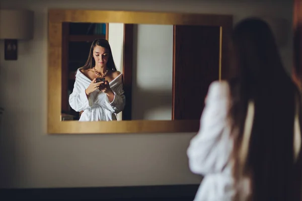 Persone, bellezza, stile di vita, tecnologia e concetto di relax - bella giovane donna in accappatoio bianco con smartphone che chiama e parla alla spa. — Foto Stock