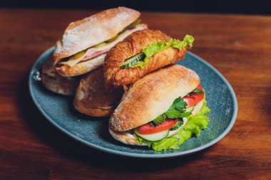 İnce dilimlenmiş jambon, salam ve taze yeşil marul ya da fesleğenle dolu çeşitli lezzetli baget sandviçler eski ahşap bir masanın üzerinde sıralanmış.