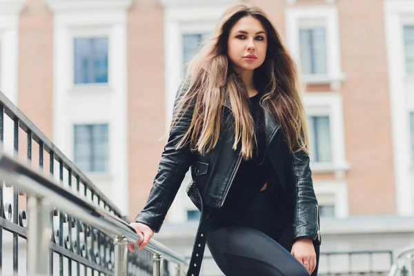 Uma linda garota loira em roupas casuais urbanas no estilo de vida contra o fundo de uma casa preta geométrica. — Fotografia de Stock