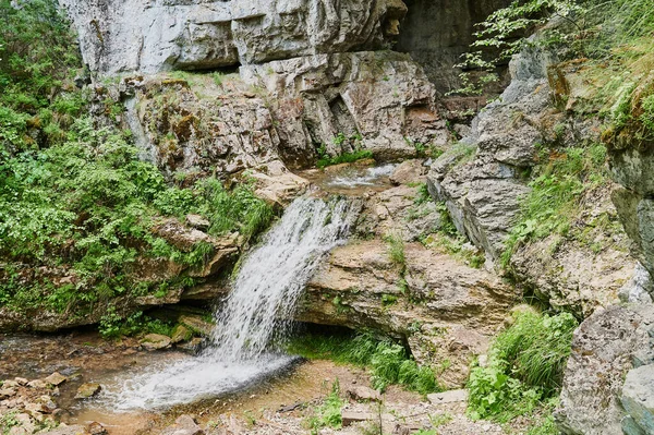 Vista de uma pequena cachoeira de rio de montanha entre grandes paralelepípedos de um penhasco. — Fotografia de Stock