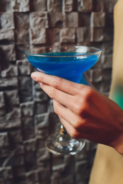 Een meisje houdt in haar hand een doorzichtig glas blauwe cocktail, ijsblokjes drijven in het glas. — Stockfoto