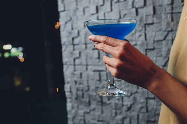 Дівчина тримає в руці прозорий келих блакитного коктейлю, кубики льоду плавають у склянці . — стокове фото