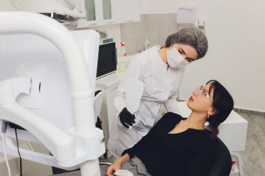 Diş hekimi ve hasta, arka planda tıbbi ekipmanlarla yapılan bir muayenede tedaviyi seçiyor.