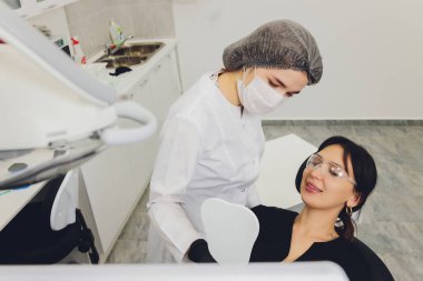 Diş hekimi ve hasta, arka planda tıbbi ekipmanlarla yapılan bir muayenede tedaviyi seçiyor.