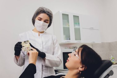 Diş hekimi ve hasta, arka planda tıbbi ekipmanlarla yapılan bir muayenede tedaviyi seçiyor.