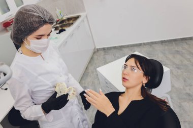 Diş hekimi ve hasta, arka planda tıbbi ekipmanlarla yapılan bir muayenede tedaviyi seçiyor.